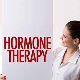 A woman in a white coat smiling and holding a sign that reads 'HORMONE THERAPY'.